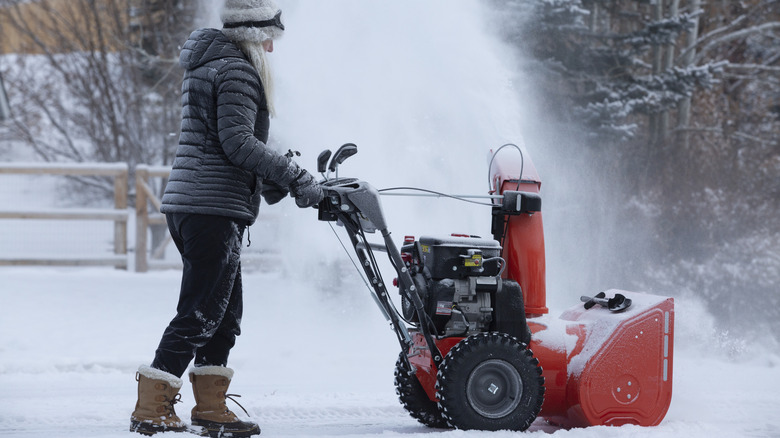 Person in winter clothes pushing snow blower