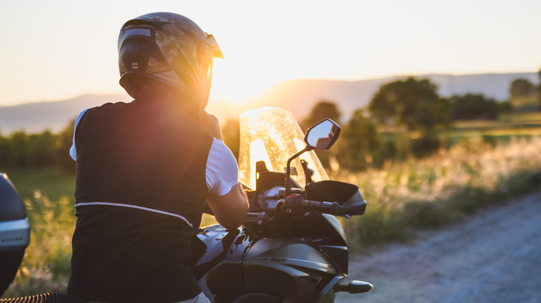 A man wearing a helmet properly before hitting the road on his motorcycle upon sunset