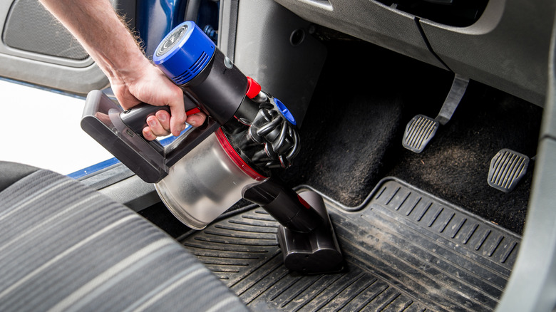 person vacuuming car floor mats