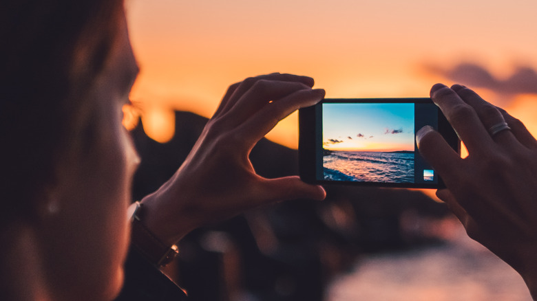 A woman clicking a picture on an iPhone by holding it in both hands