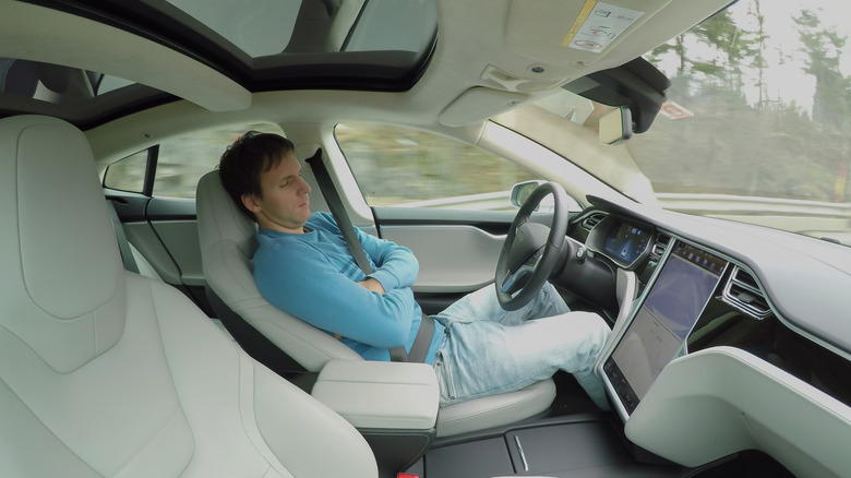 Man in jeans and blue shirt sleeping behind wheel of fully autonomous car