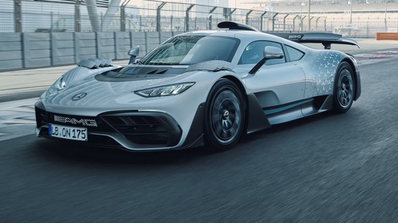 Silver Mercedes AMG-one driving on race track near curb and catch fence