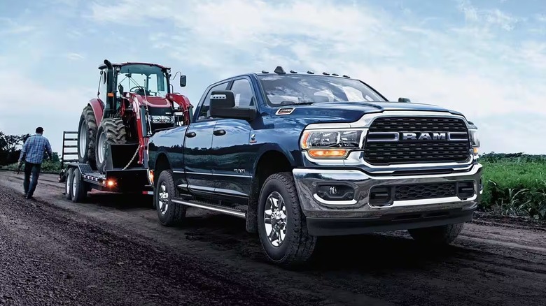 A Ram 2500 truck pulling a trailer loaded with a farm tractor on a muddy road