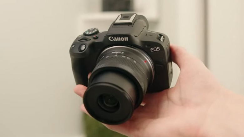 A hand holding a Canon EOS R50 camera.