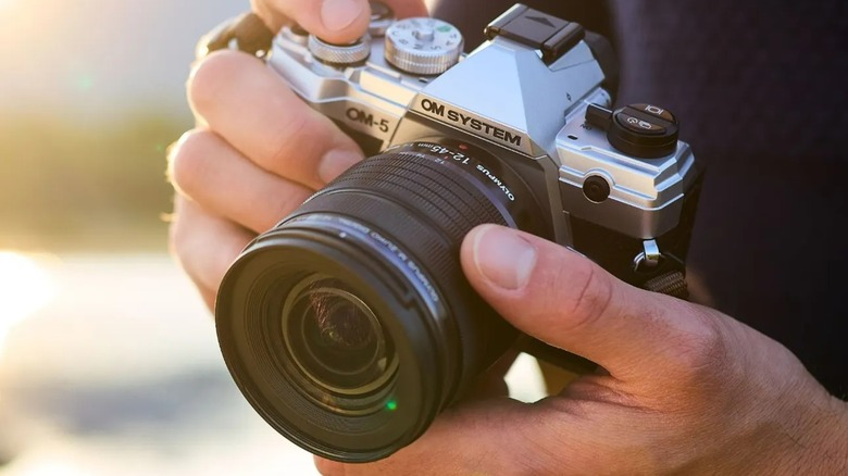 A person holding an OM-5 camera outside.