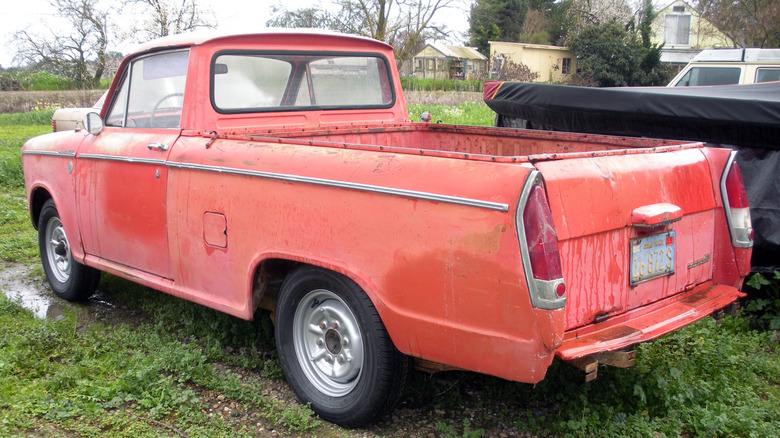 faded red Datsun NL320 pickup truck parked  in field