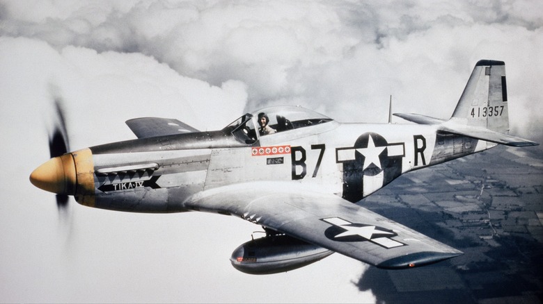 P-51 Mustang in flight above clouds with ground visible below