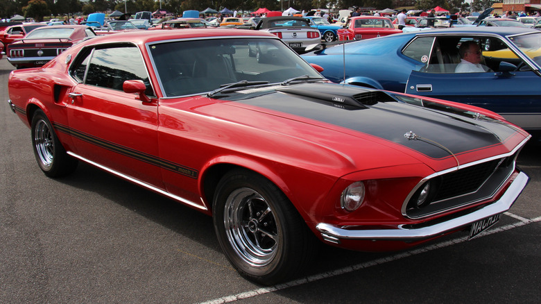 Red and black 1969 Ford Mustang sportsroof parked on asphalt lot at car show