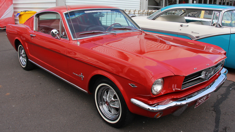 red 1965 Ford Mustang fastback parked at classic car dealership