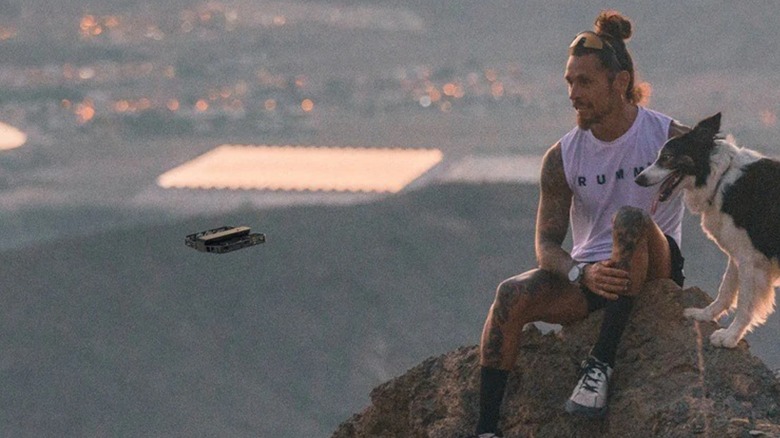 A hiker and his dog being photographed by a HoverAir drone high on a hill