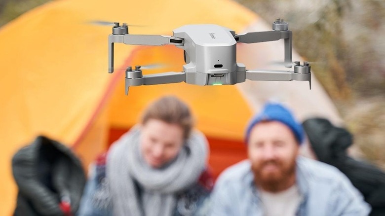 Couple sitting in front of tent flying a Potensic Atom SE drone at a campsite