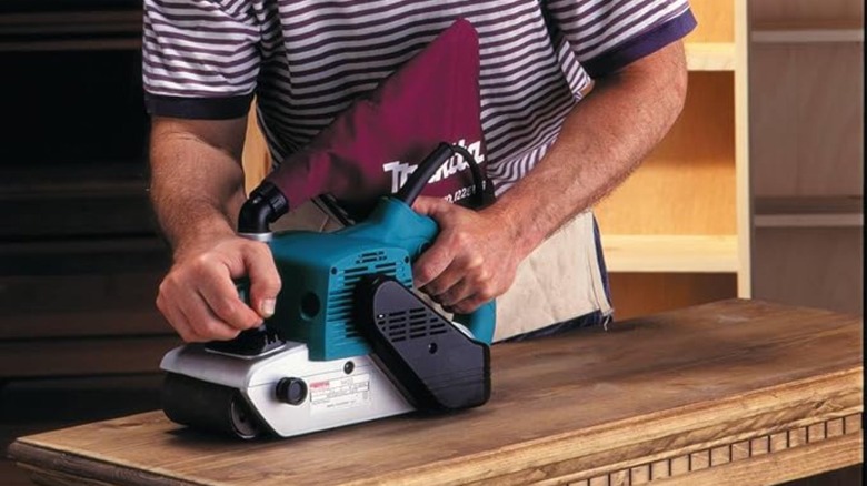 Man in striped shirt using a belt sander on a table