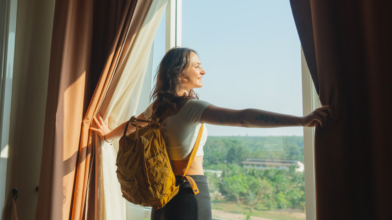 Woman draws curtains in a hotel room