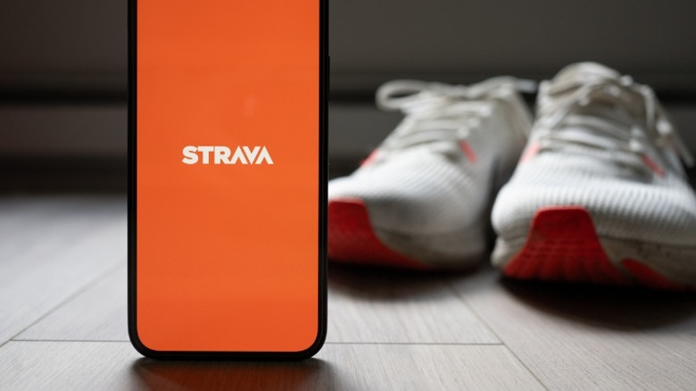 Strava app logo on a phone next to a pair of shoes