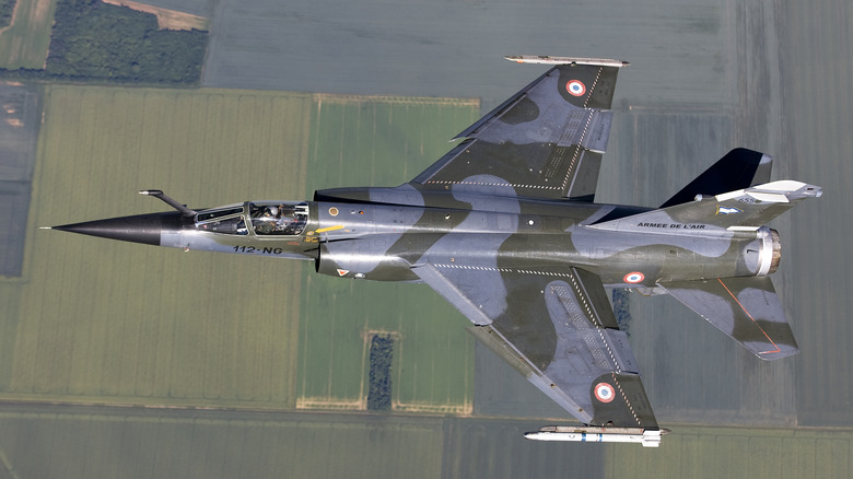 A camouflage-painted Mirage F1 flies over farmlands