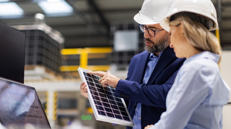 A worker in a solar panel factory holds part of a panel as his colleague looks on with a smile