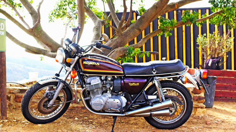 Purple Honda CB750 parked in dirt in front of tree