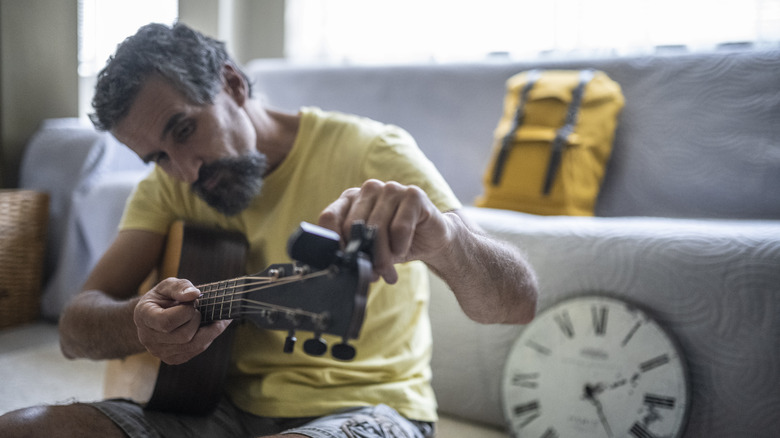 man tunes guitar using tuner