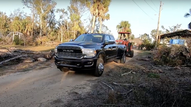 Black 2019 Ram truck pulling trailer with red farm tractor on dirt road