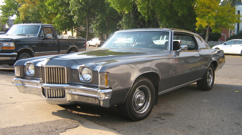 grey Pontiac Grand Prix parked in street with ford pickup truck and trees in background