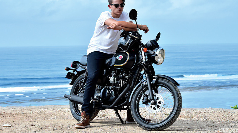 Person posing on Kawasaki W175 parked at beach