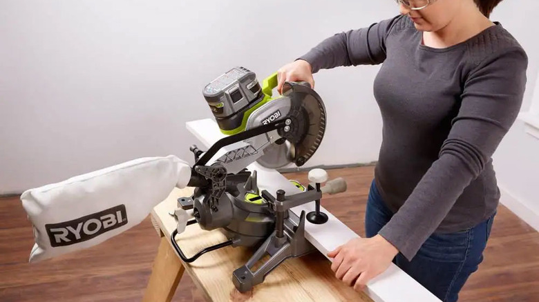 woman using a Ryobi miter saw to cut white boards