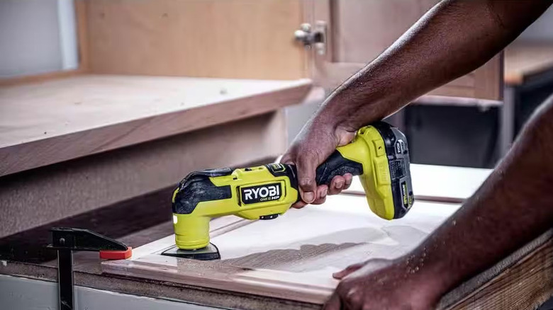 man using Ryobi cordless multitool to sand corner