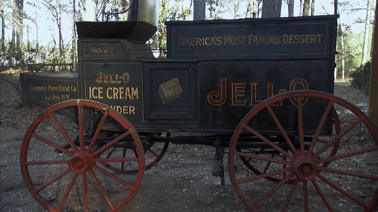 Horse-drawn Jell-O wagon parked outside barn with Mike Wolfe and owner looking on