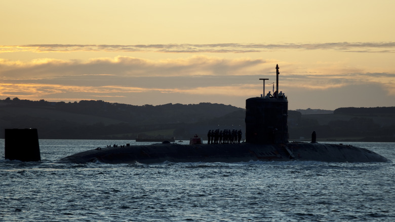 A military submarine's silhouette on the water's surface with a sunset in the background