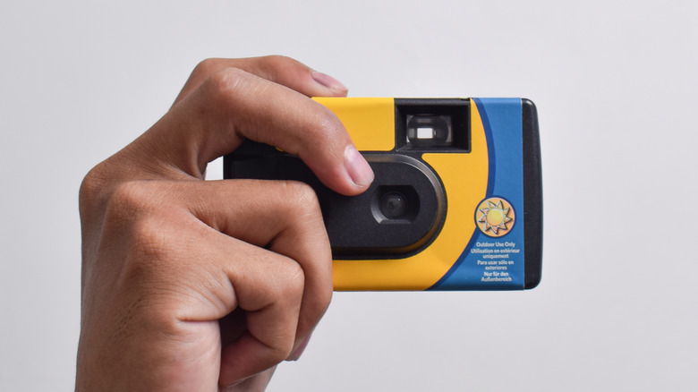 A hand holding a disposable camera.