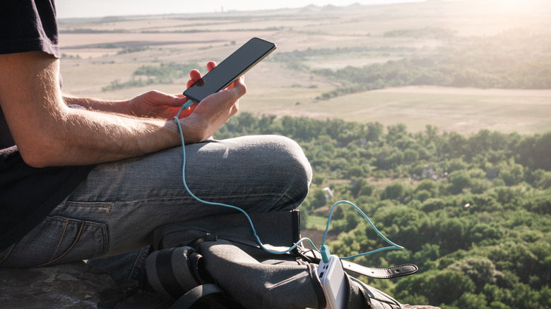 man charging smartphone with power bank outdoors