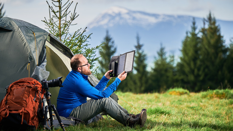 man sitting by tent holding e-reader