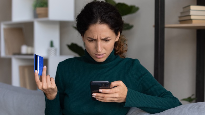 Woman in turtleneck holding credit card and smartphone.