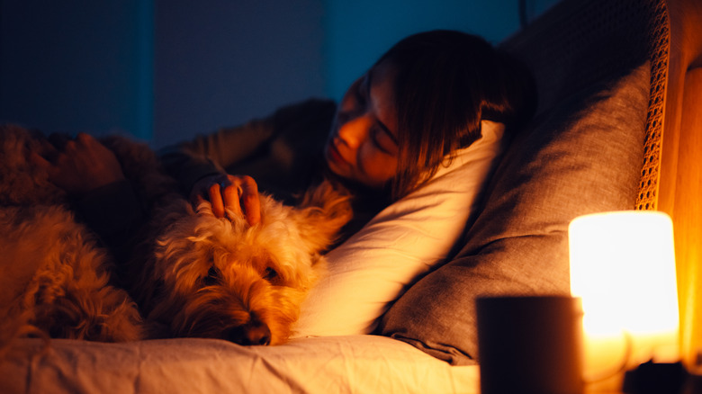 Woman in bed with dog next to cozy light