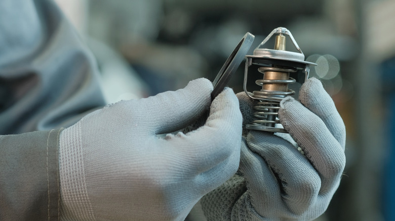 An auto mechanic holds a thermostat