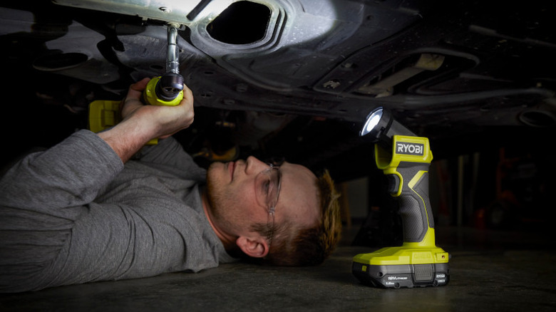 Mechanic using Ryobi 18V One+ LED Flashlight while working under a car