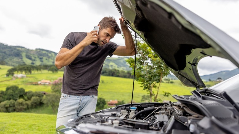 A person with a broke down car listening to the engine