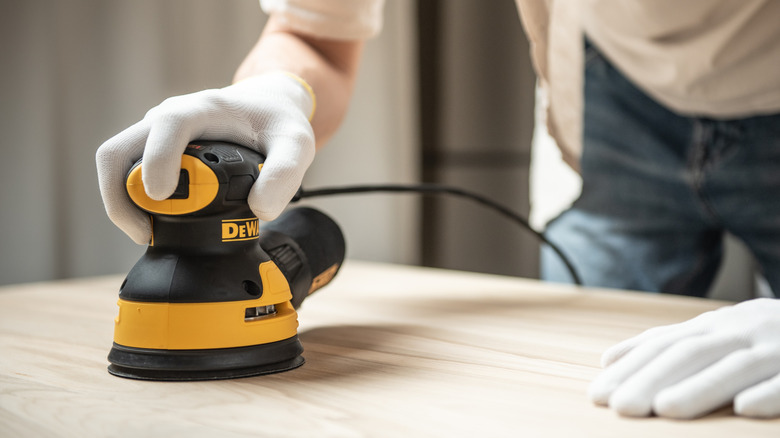 Man using DeWalt orbital sander on wooden surface