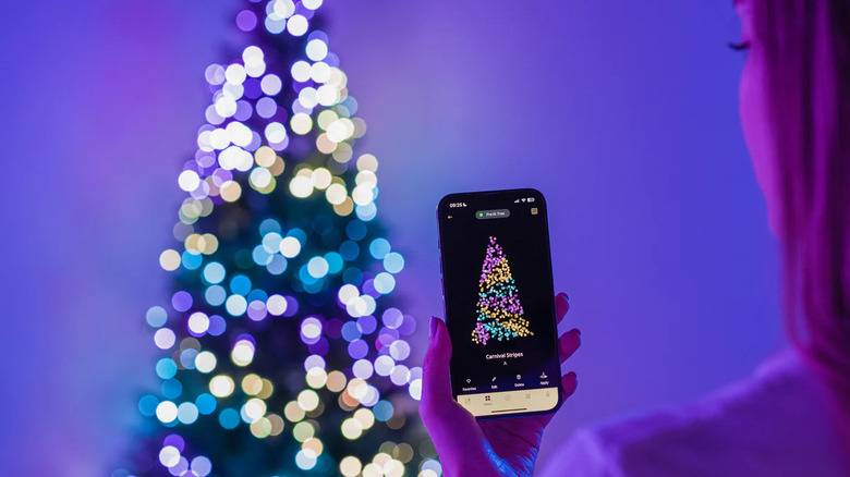 A person holds a smartphone to adjust LED lights on a Christmas tree