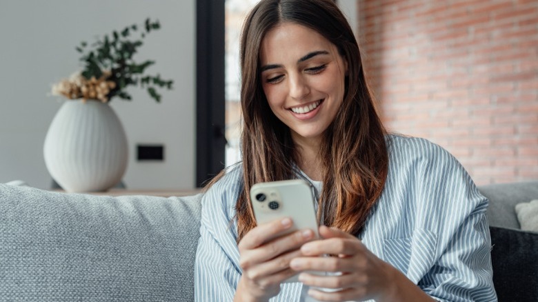 A smiling woman using her phone on the couch