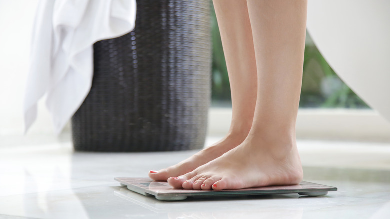 A faceless woman is standing on top of a bathroom scale