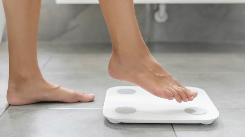 A faceless person is getting on a bathroom scale