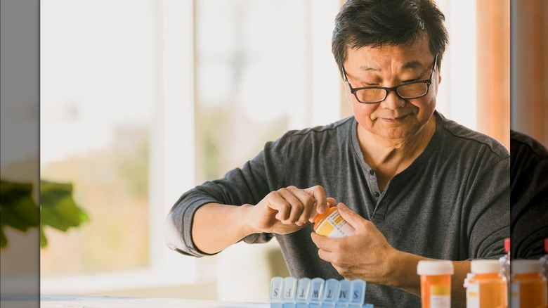 man sorting pill bottles into daily pill box