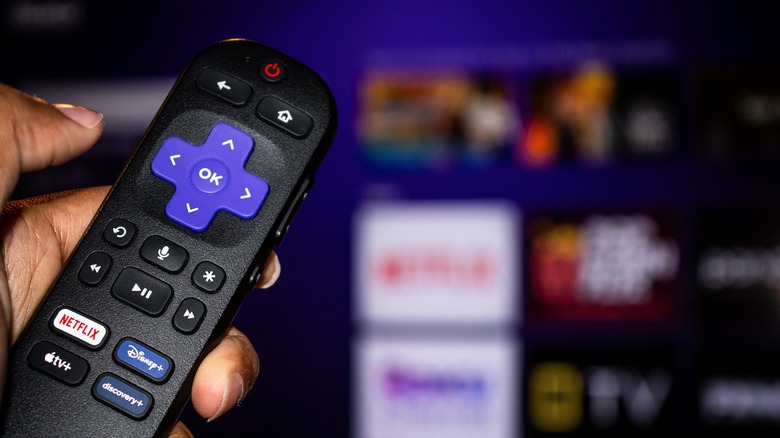 The Roku TV remote in front of a Roku compatible TV