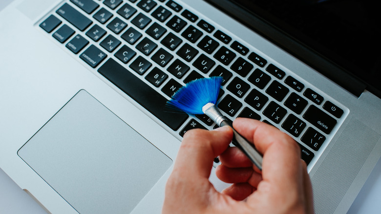 person cleaning laptop keyboard with brush