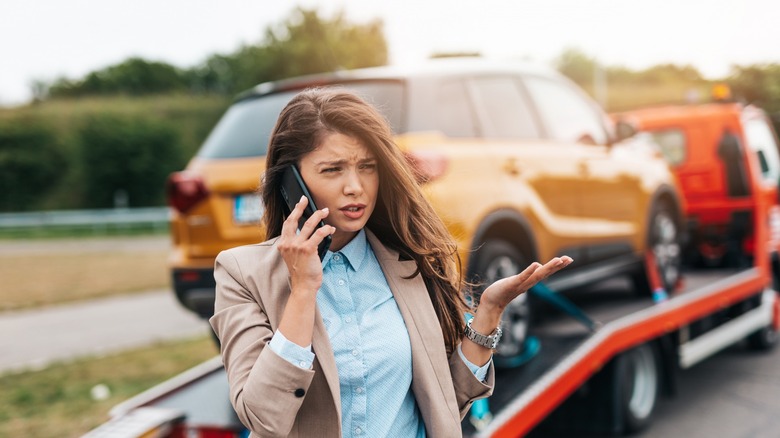 woman on phone with car on wrecker