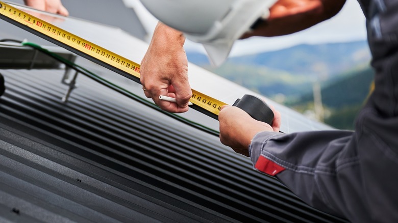 Man measuring solar panel on roof