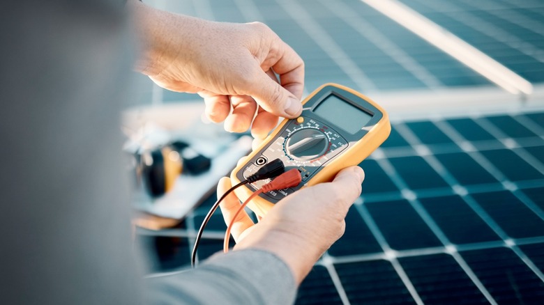 Person holding a multimeter to a solar panel