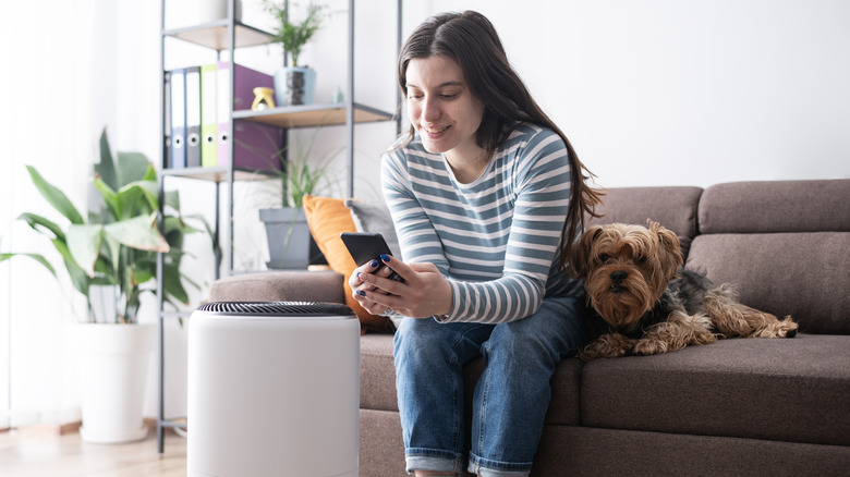 Woman controlling air purifier next to dog