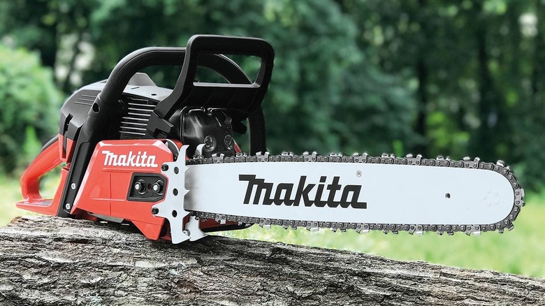 An orange Makita chainsaw on top of a fallen tree.